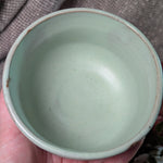 mint green matcha tea bowl held in a hand against a brown fabric background