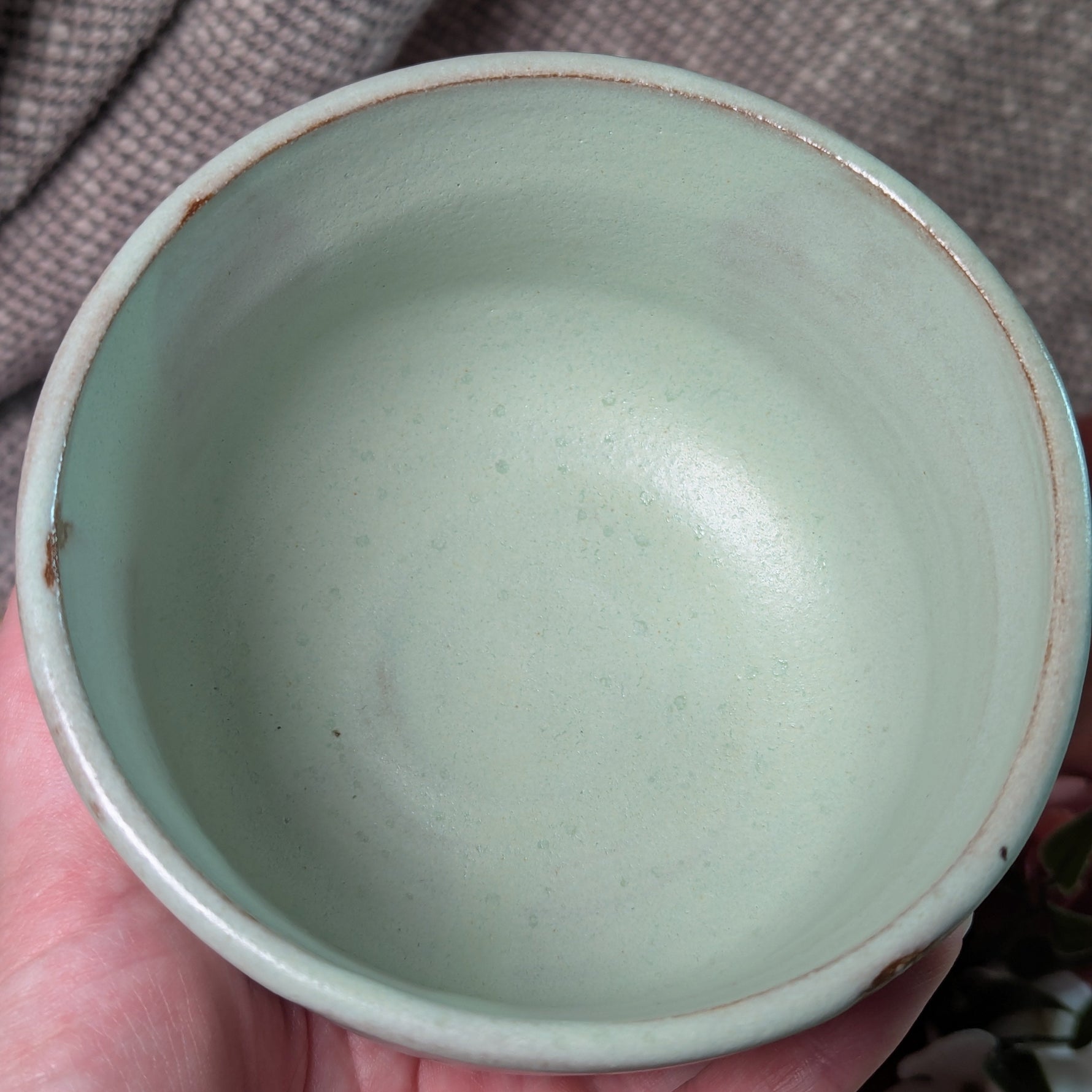 mint green matcha tea bowl held in a hand against a brown fabric background