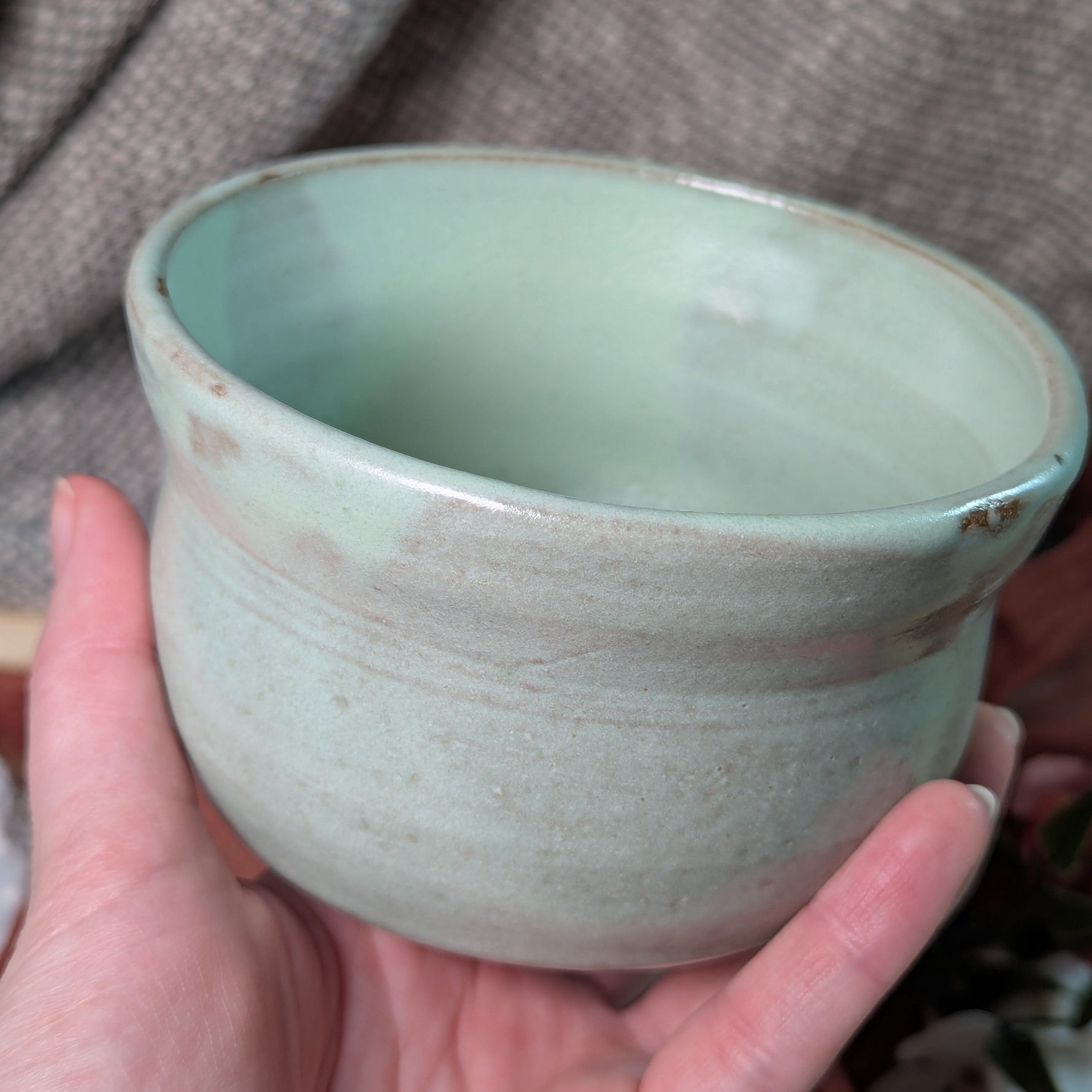 Hand holding a mint green matcha tea bowl against a gray background