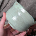 Mint green matcha tea bowl held by a hand against a textured gray background