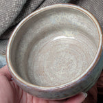 Hand holding a ceramic bowl with a textured surface against a fabric background