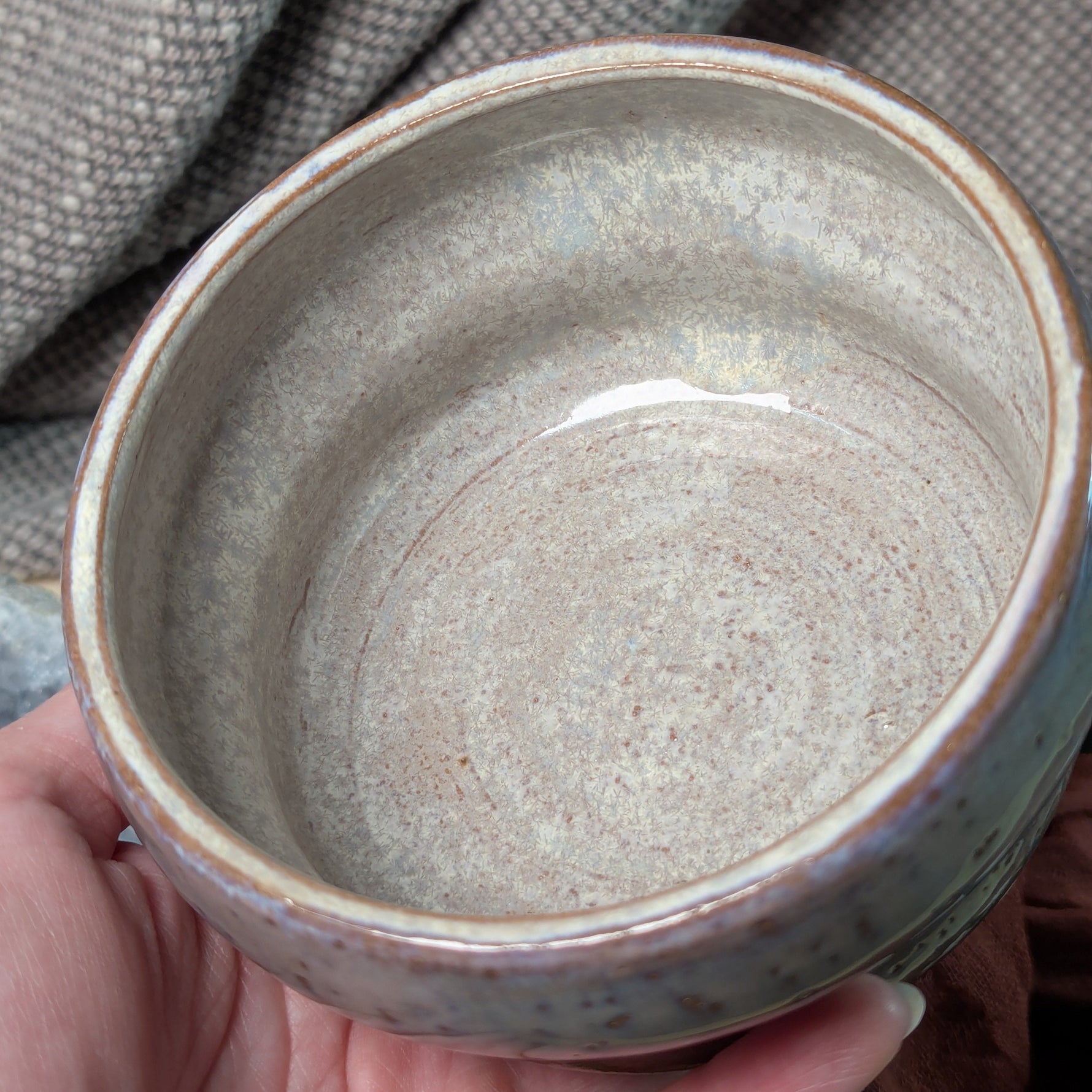 Hand holding a ceramic bowl with a textured surface against a fabric background