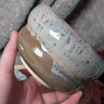 Hand holding a ceramic bowl with a textured surface against a gray fabric background