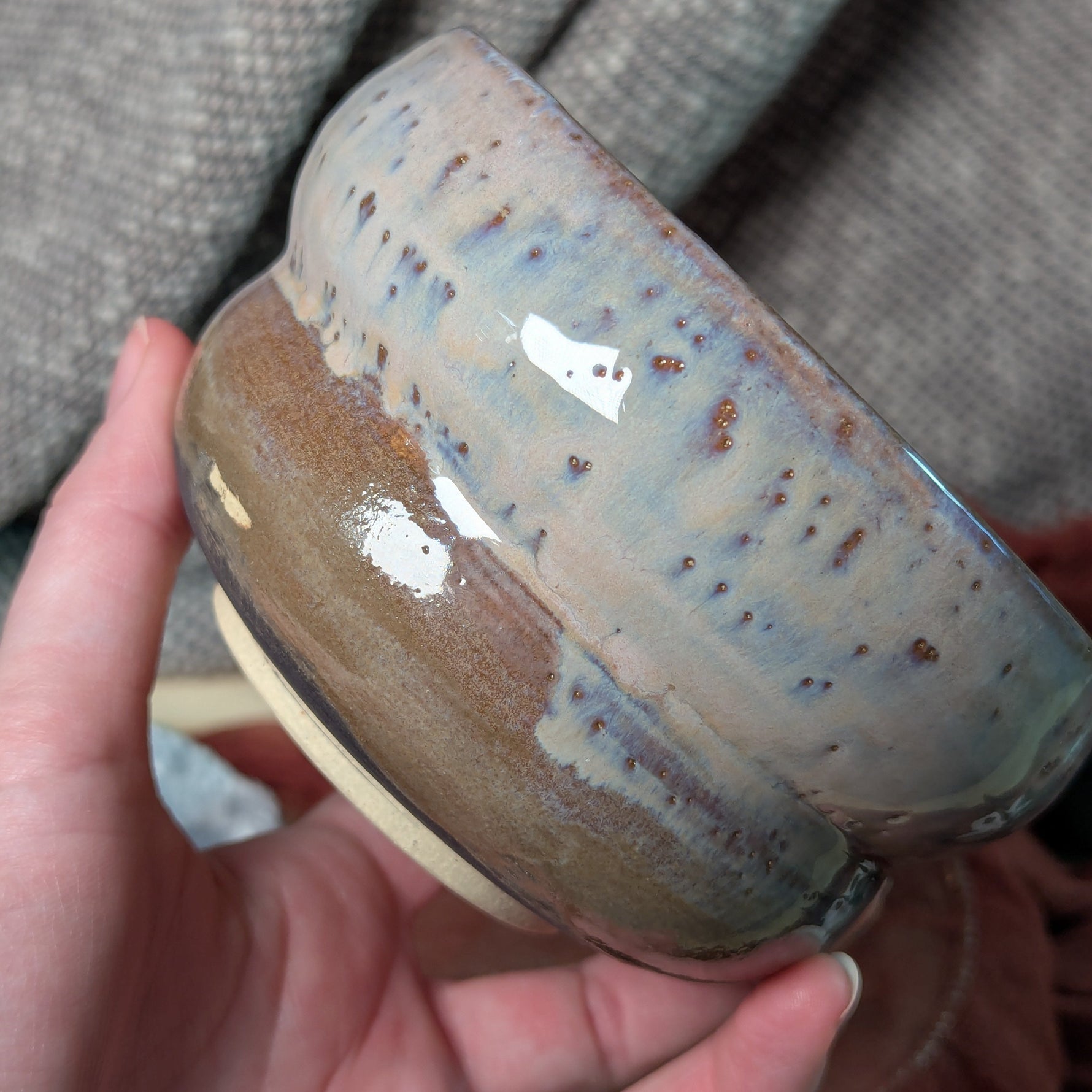 Hand holding a ceramic bowl with a textured surface against a gray fabric background