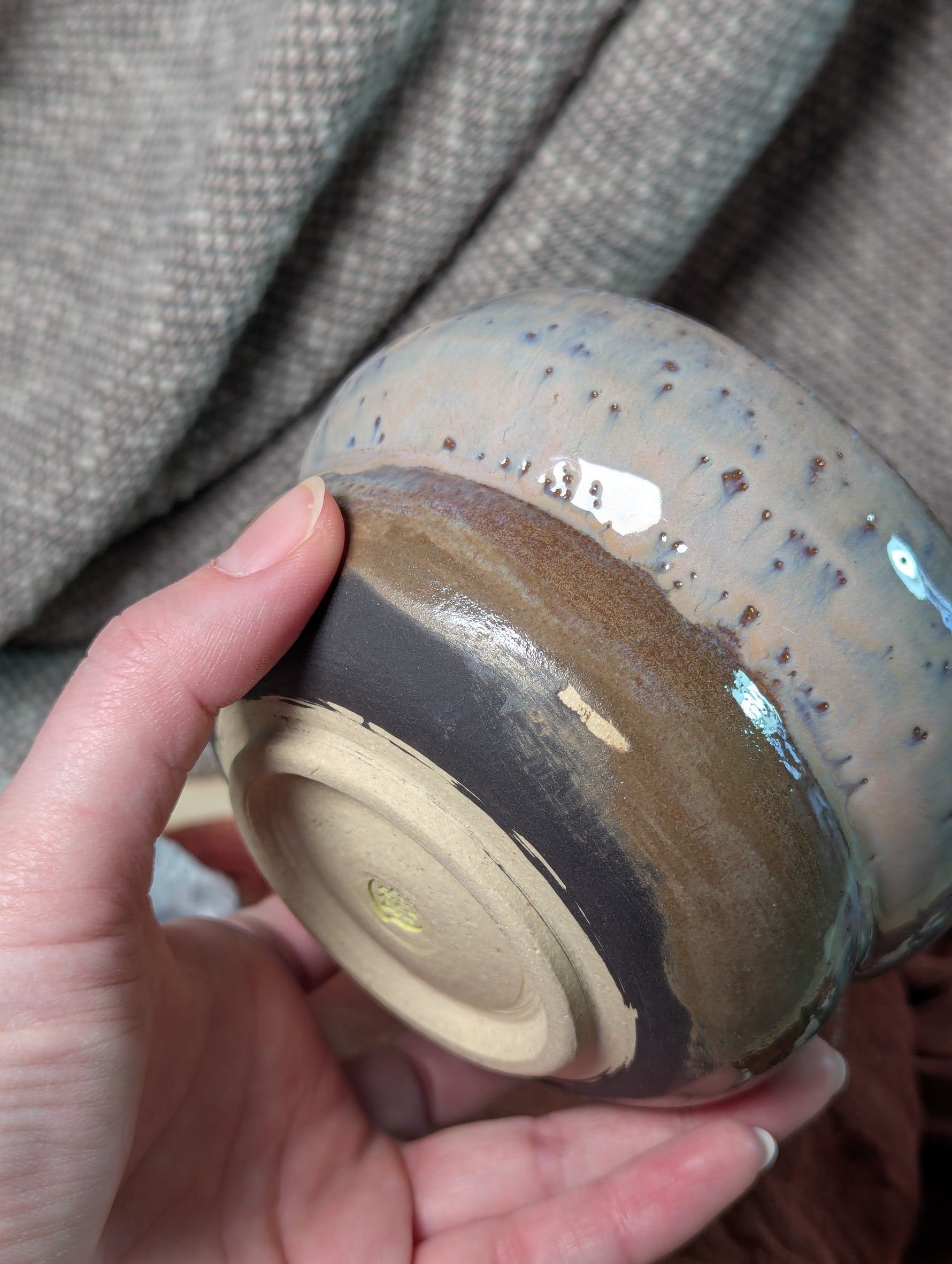 Hand holding a ceramic bowl with a textured surface against a fabric background