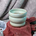 mint green ceramic cup on a textured surface with a blurred background