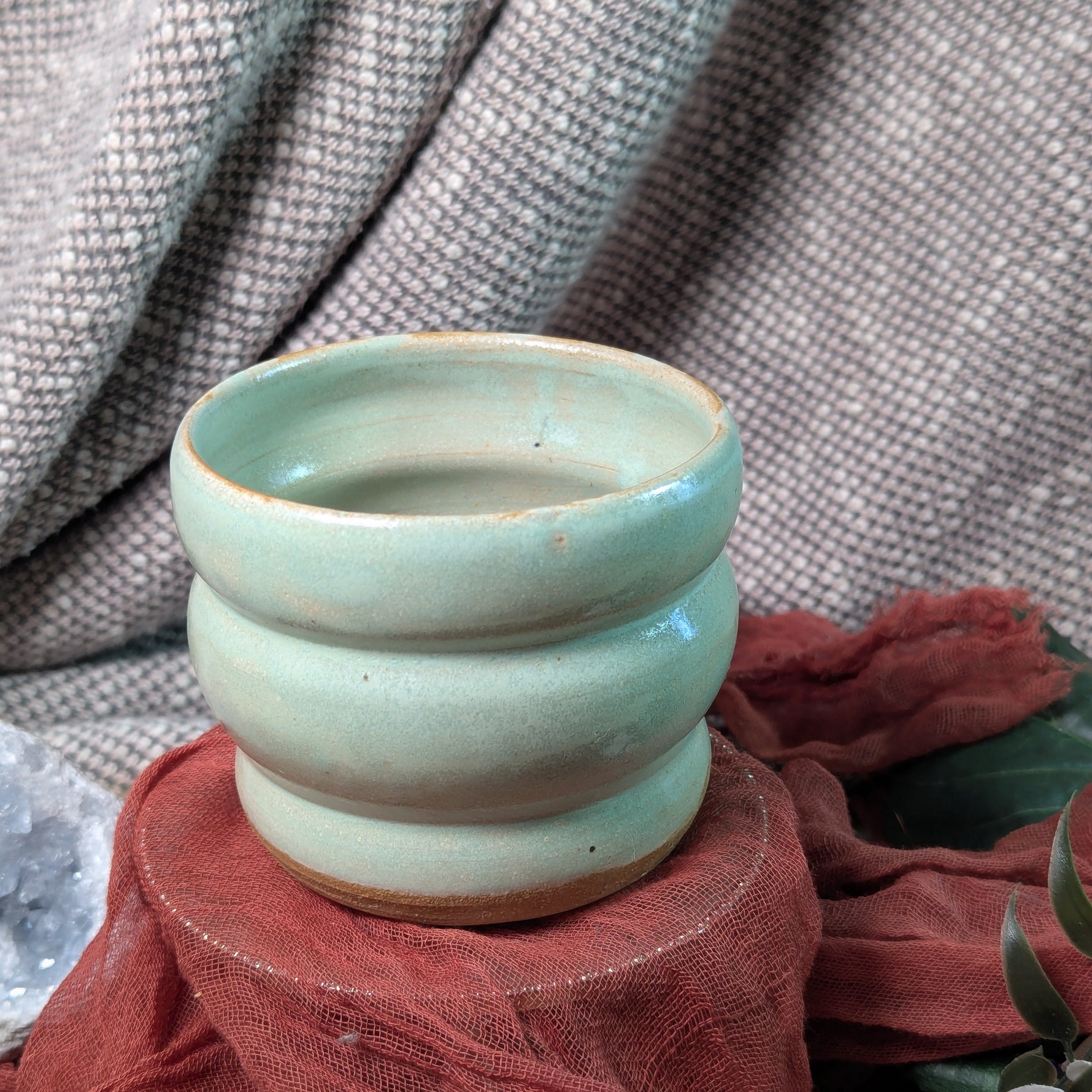 mint green ceramic cup on a textured surface with fabric and flowers