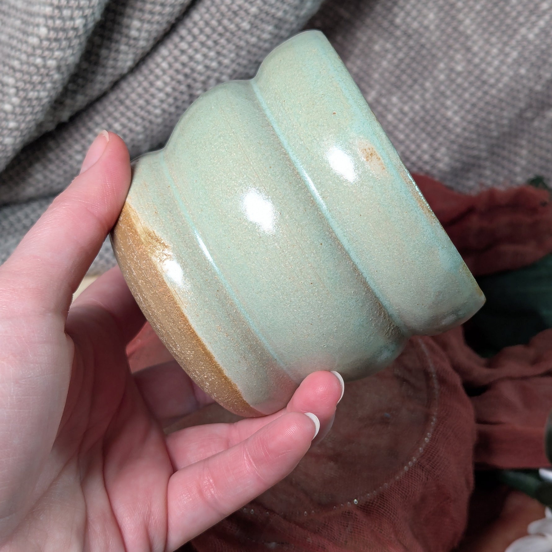 Hand holding a mint green ceramic cup against a textured gray background