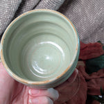 Hand holding a mint green ceramic cup against a textured fabric background