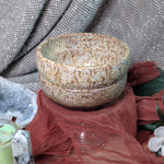 Speckled ceramic bowl on a textured surface with fabric and flowers