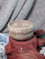 Speckled ceramic bowl on a textured surface with a floral arrangement