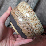 Hand holding a ceramic bowl with speckled design against a textured gray background