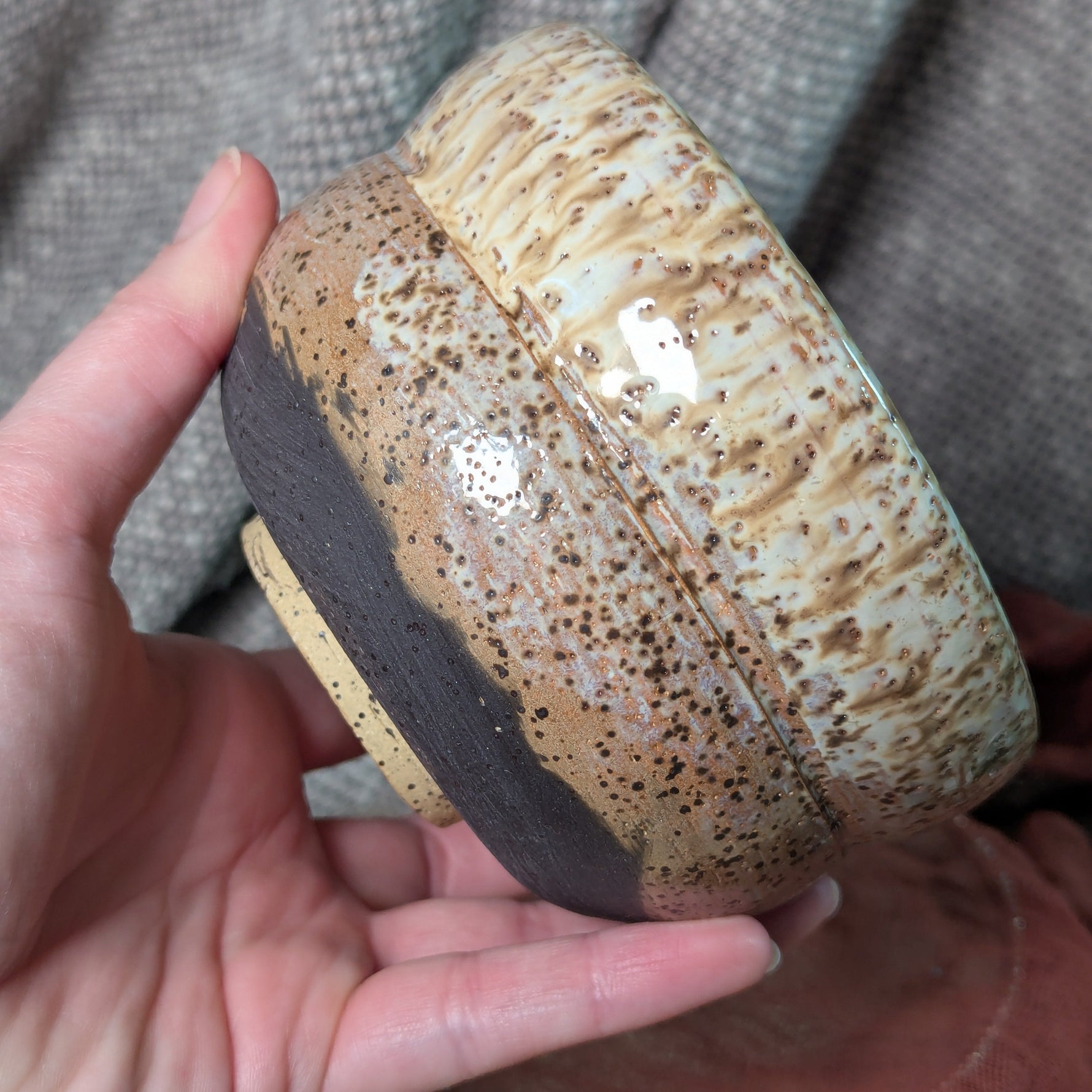 Hand holding a ceramic bowl with speckled design against a textured gray background