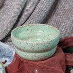 Green ceramic bowl with speckled texture on a textured fabric background