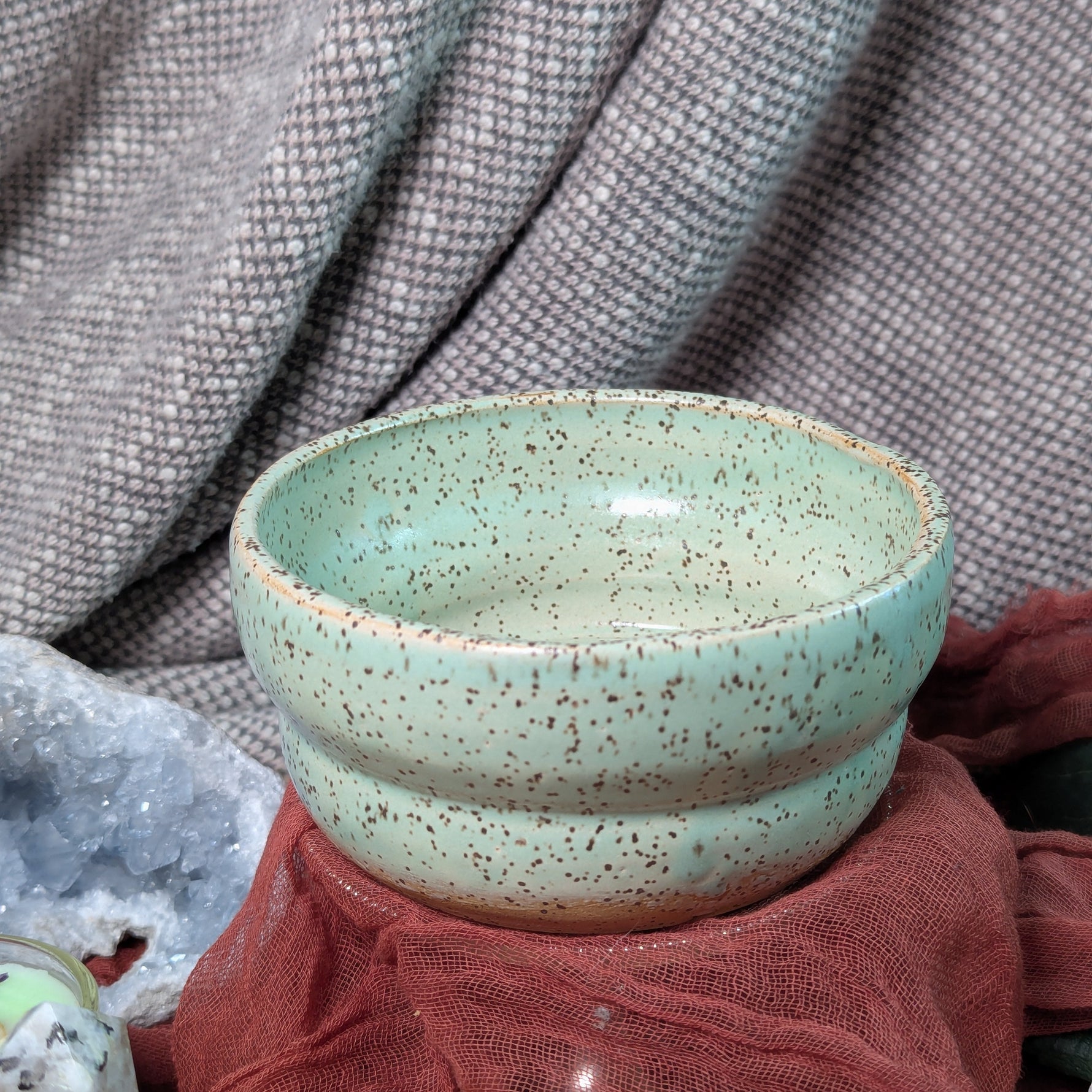 Green ceramic bowl with speckled texture on a textured fabric background