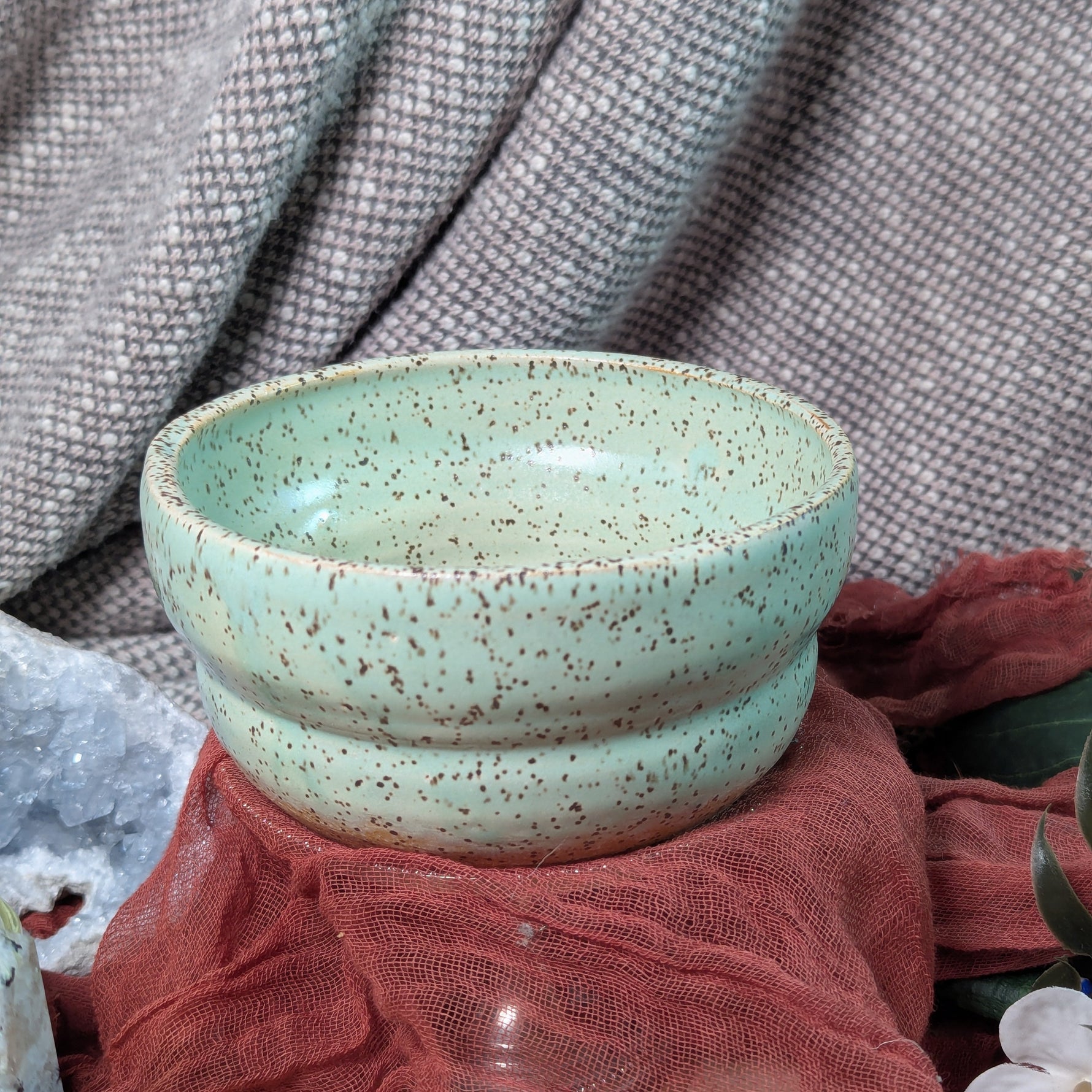 Speckled green ceramic bowl on a textured surface with a blurred background