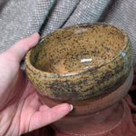 Hand holding a ceramic bowl with speckled pattern against a textured fabric background